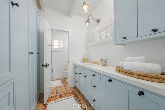 Bathroom with pale blue cabinetry, a long white counter, and folded towels in a woven basket.