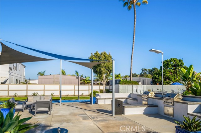 Outdoor patio with built-in grill, shade sails, dining set, and a glimpse of the pool.