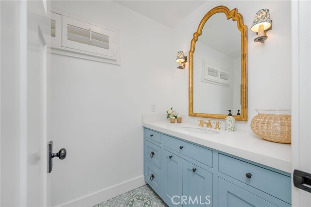 Bathroom with pale blue vanity, ornate gold-framed mirror, and patterned floor tile.