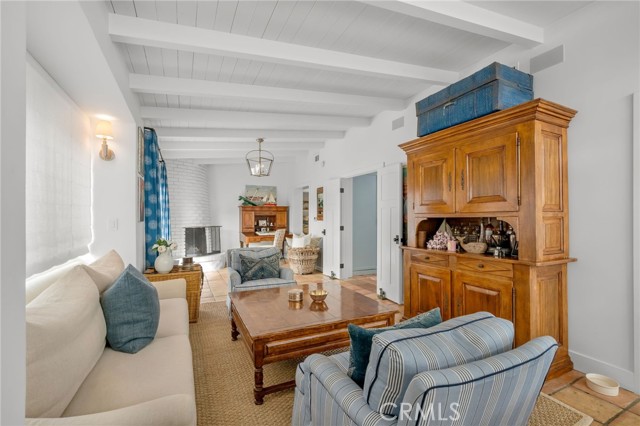 Living room with exposed ceiling beams, blue-striped armchairs, and a large wooden hutch.
