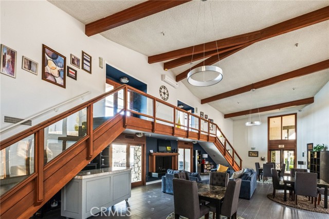 Open-plan living area with a wood mezzanine staircase, exposed ceiling beams, kitchen and dining space.