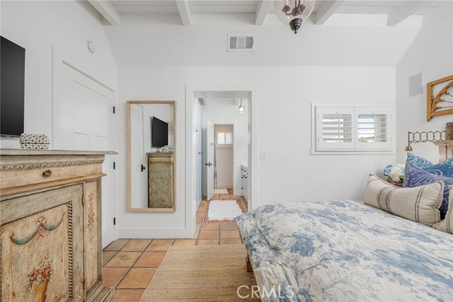Bedroom with a floral bedspread, terracotta tile floor, and white ceiling beams.