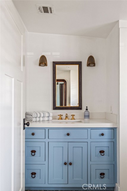 Bathroom vanity with pale blue cabinetry, brass faucets, folded towels, and a framed mirror.