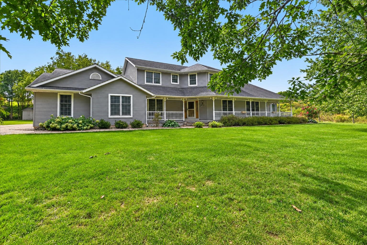 Gray two-story house with a long covered porch and broad green lawn.