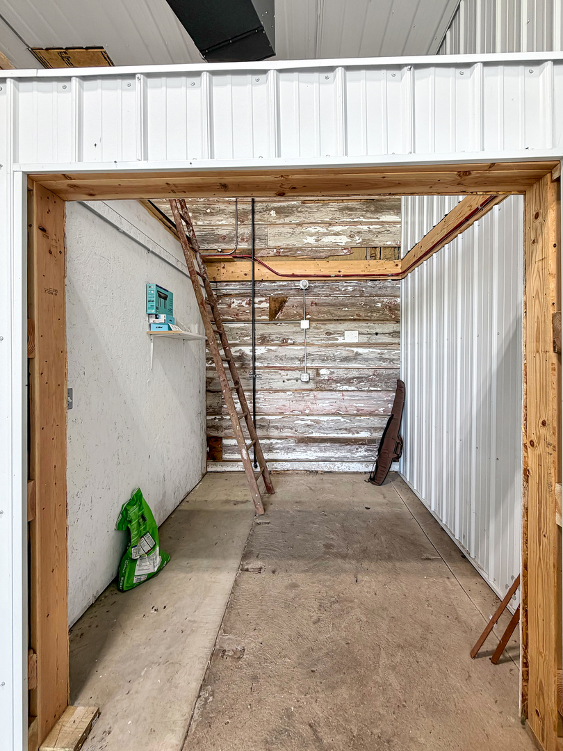 Unfinished garage interior with a concrete floor, weathered plank wall, and leaning wooden ladder.