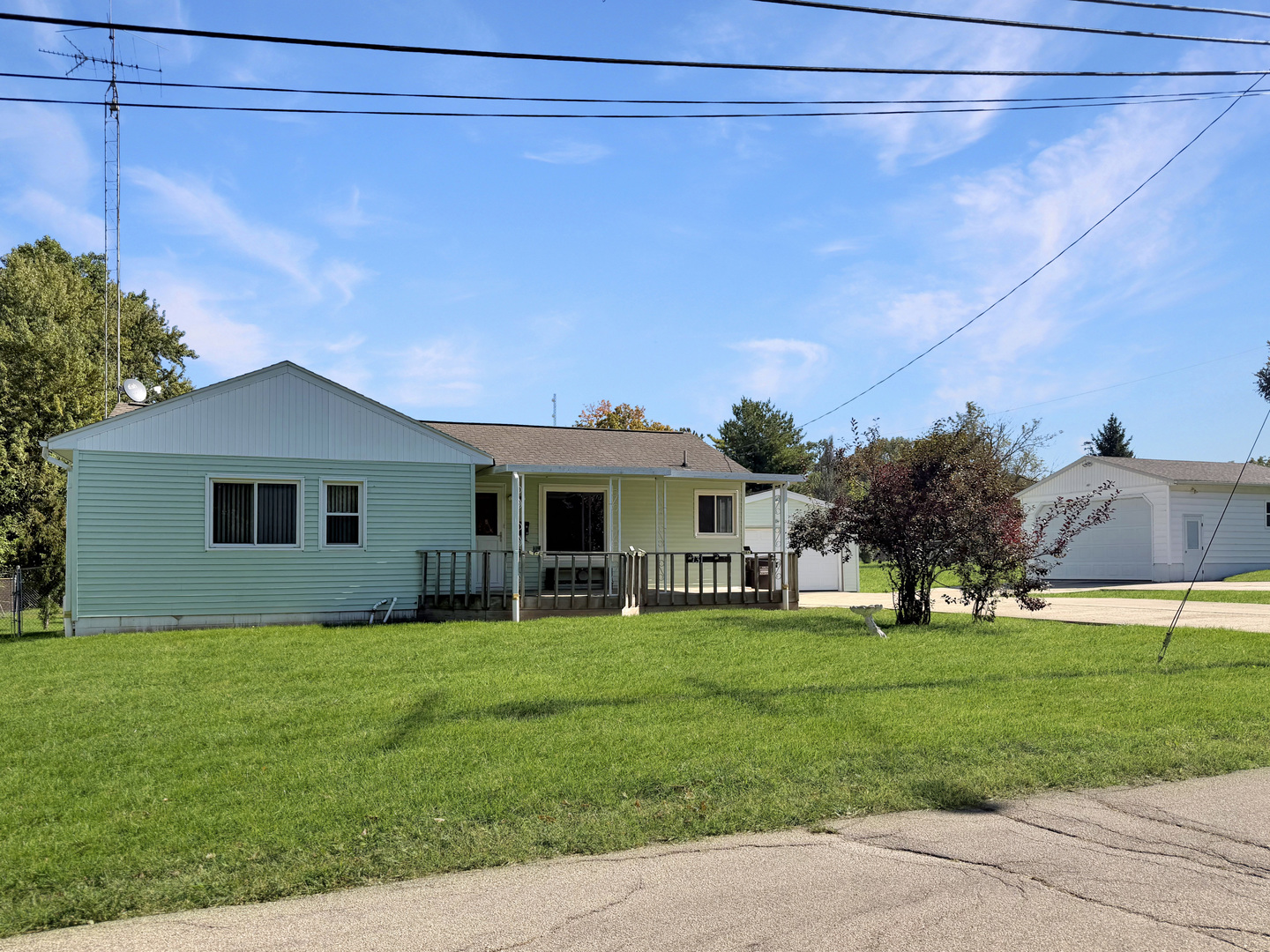 Single-story pale green home with a covered porch, broad lawn, and detached white garage.