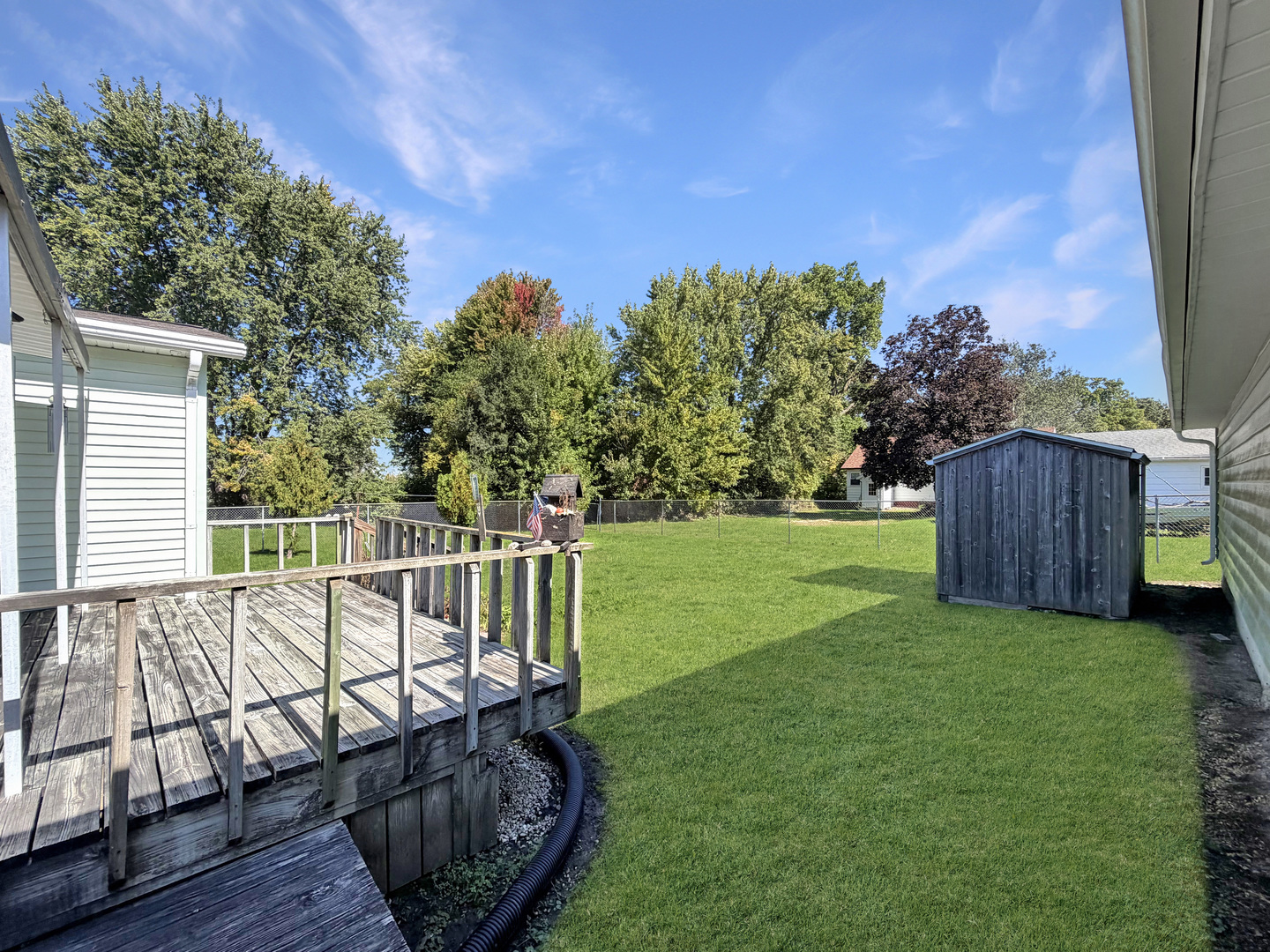 Backyard with a broad lawn, wooden deck, and dark storage shed.