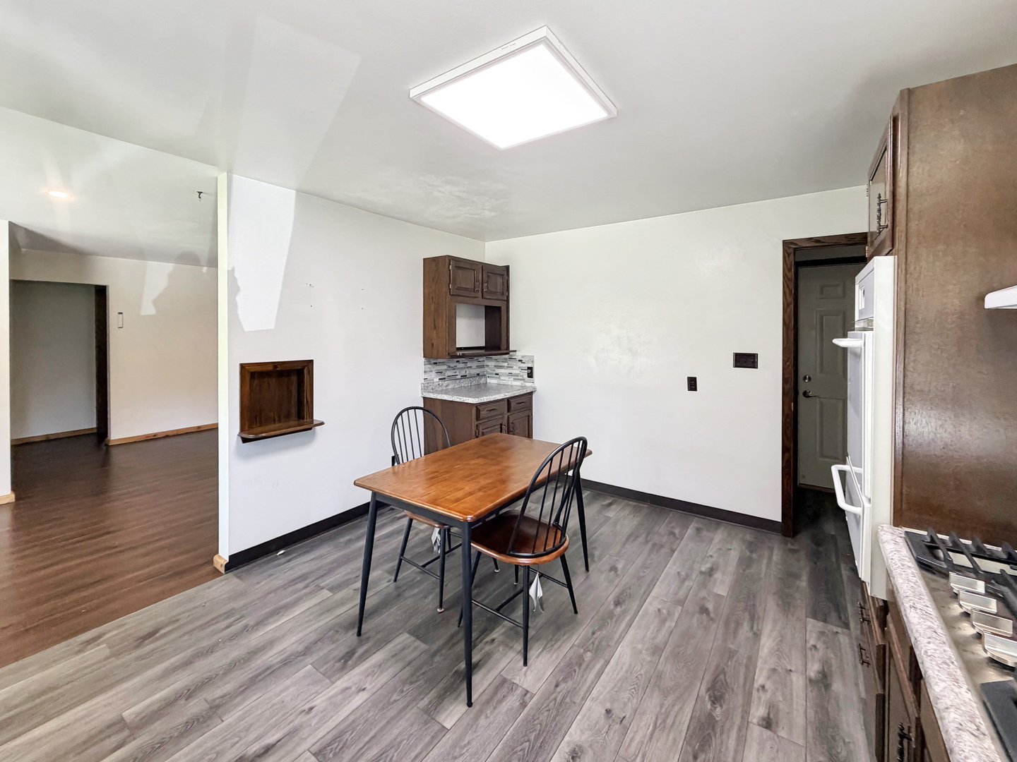 Kitchen dining area with dark wood cabinets, gray plank flooring, and a small table with chairs.