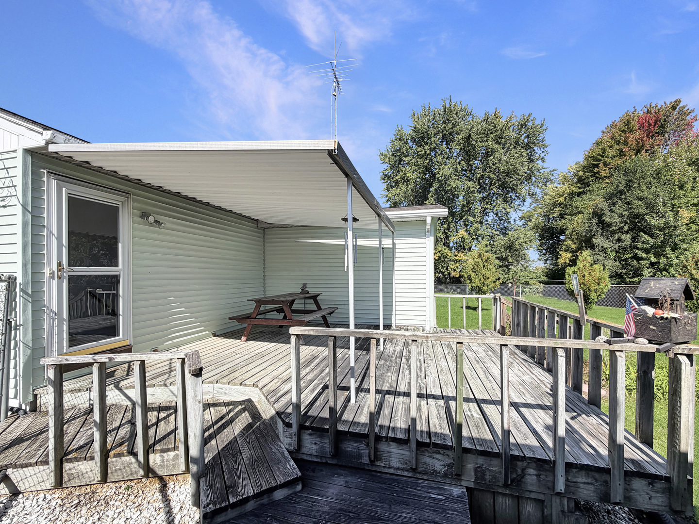 Weathered wooden deck with a covered seating area and picnic table overlooking a fenced yard.