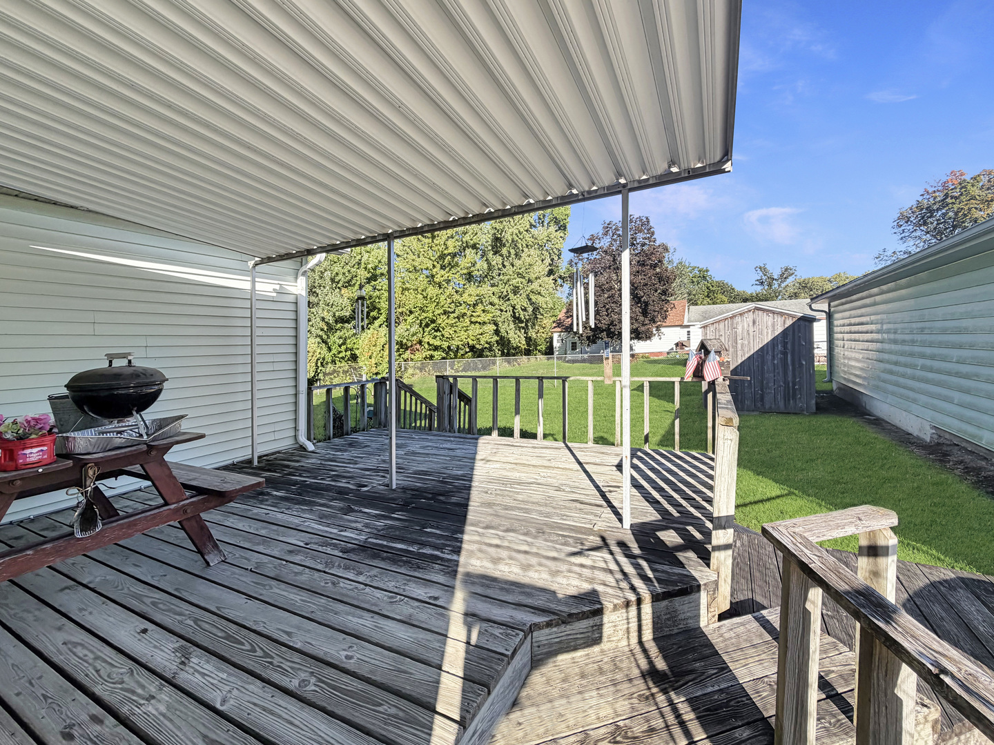 Covered wooden deck with a picnic table and grill overlooking a fenced backyard.