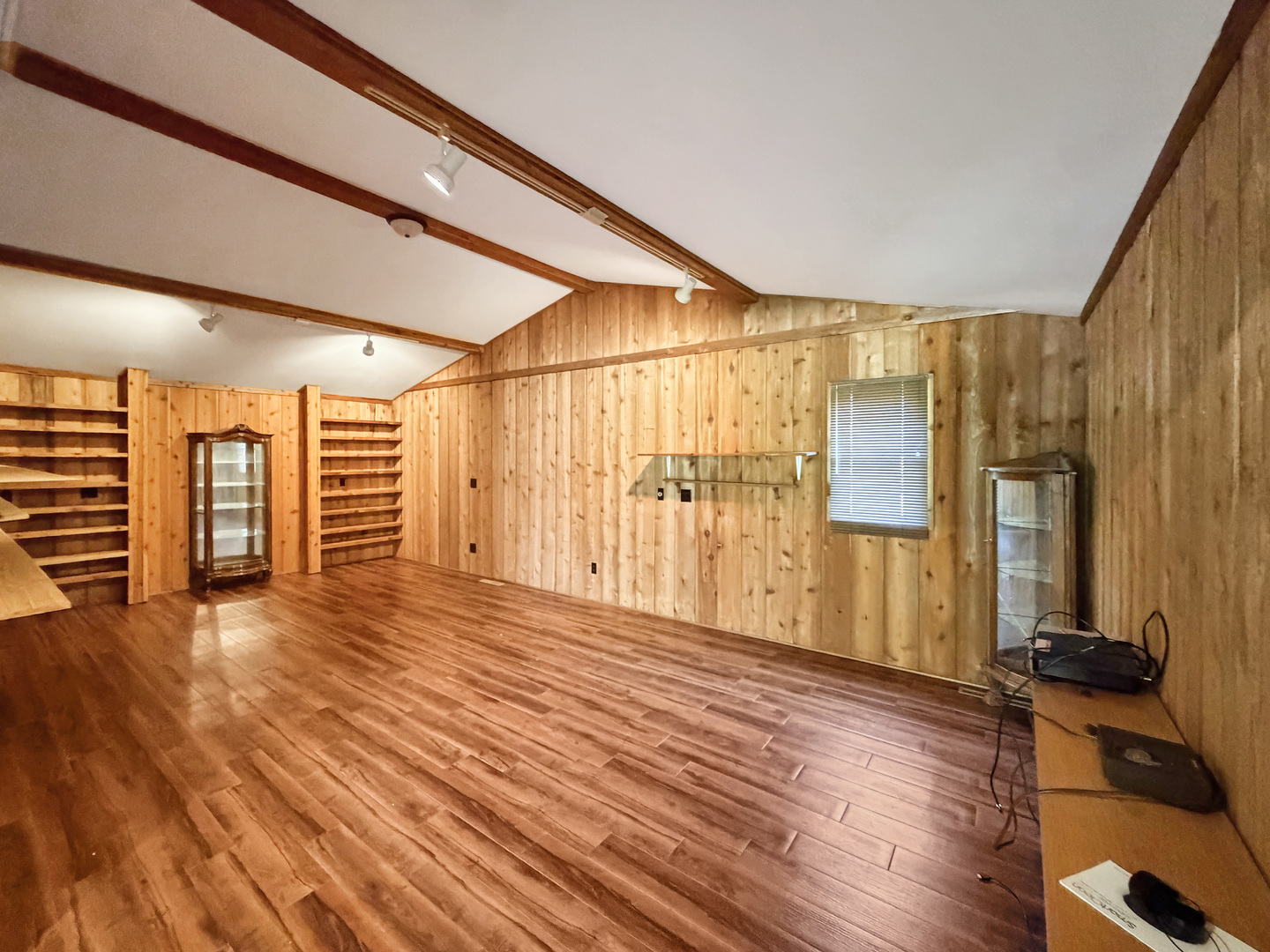 Wood-paneled room with exposed beams, built-in shelving, and wood-look flooring.
