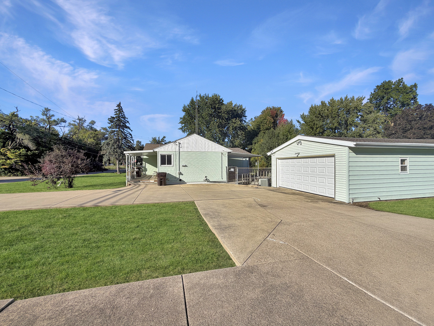 Light green single-story home and detached garage beside a broad concrete driveway.