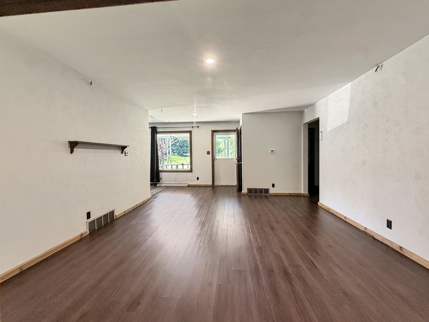 Empty living room with dark wood-look flooring and a window beside an exterior door.