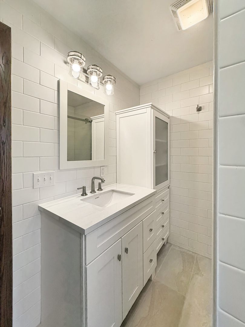 Bathroom with a white vanity, mirrored cabinet, and white tiled walls.