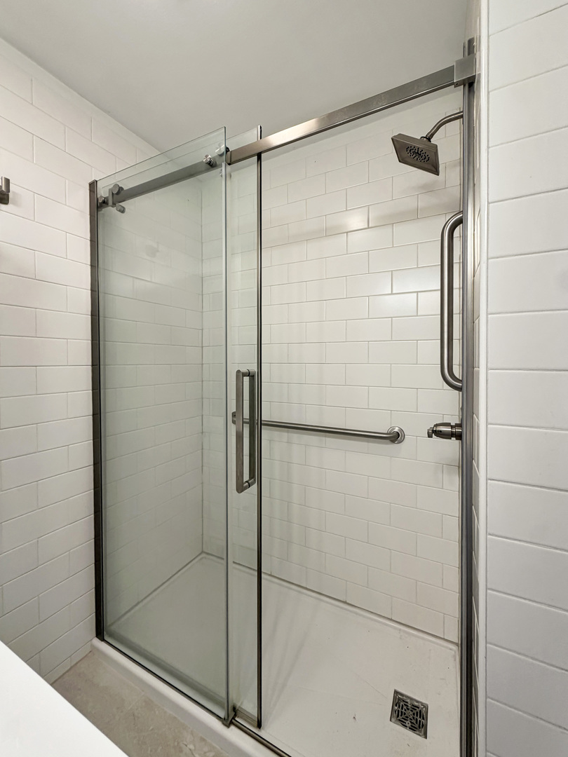 Walk-in shower with glass doors, white subway tile, and stainless steel grab bars.