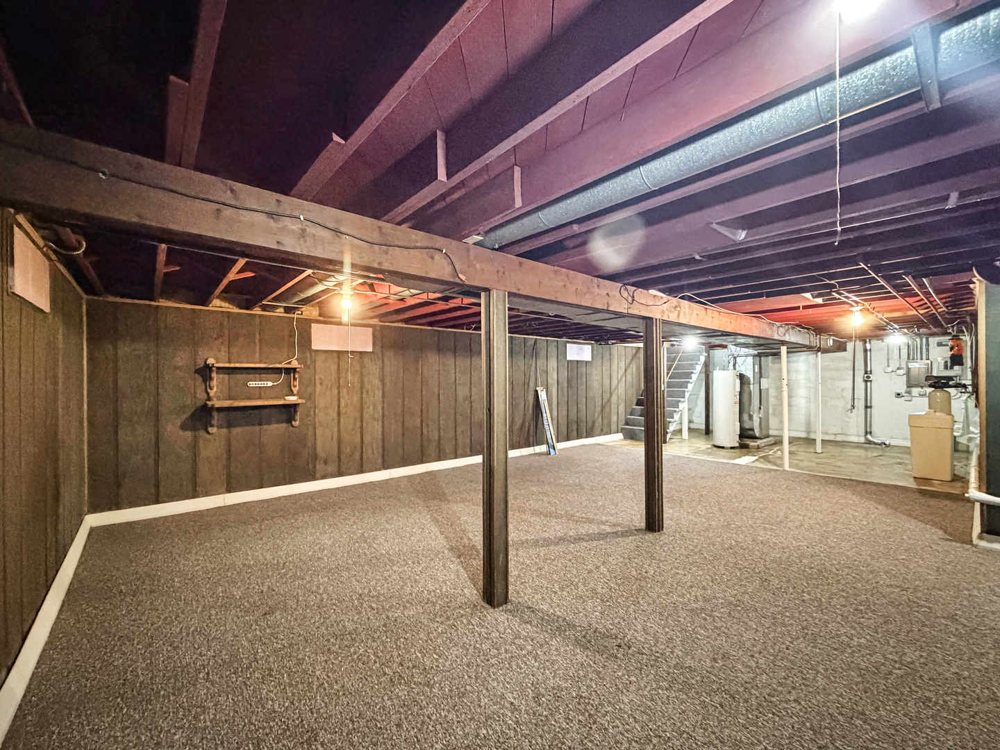 Basement with carpeted flooring, exposed ceiling joists, support posts, and utility equipment.