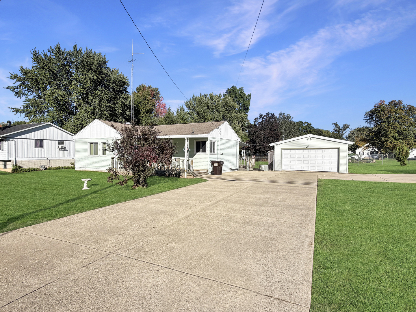 Single-story pale green house with a detached garage and broad concrete driveway.