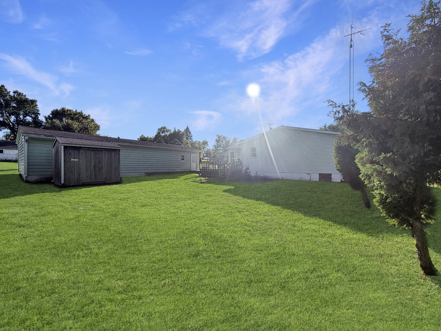 Backyard with a broad lawn, wooden shed, and mature trees beside the home.
