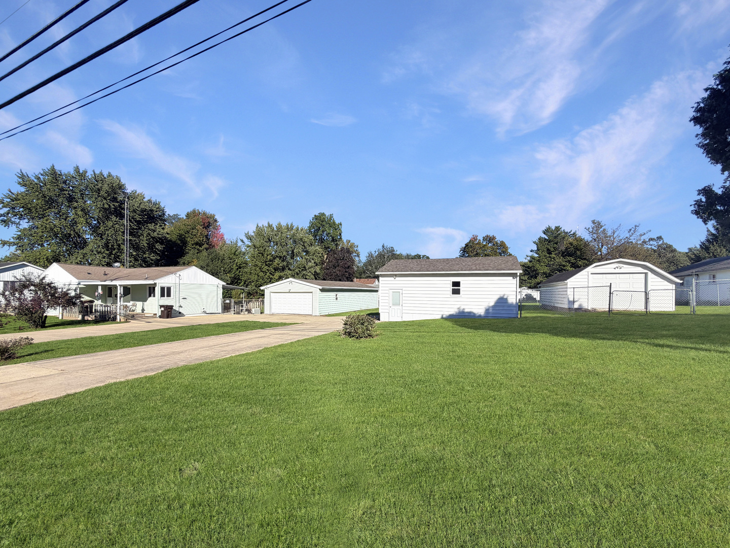 Home and detached garages beyond a broad green lawn and concrete driveway.