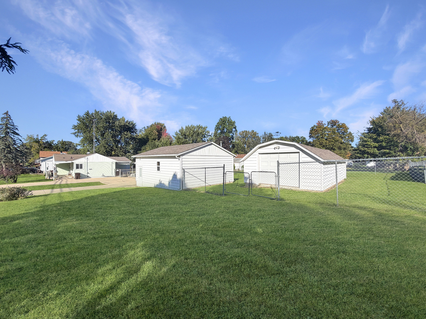 Rear yard with a broad lawn, two white detached garages, and chain-link fencing.