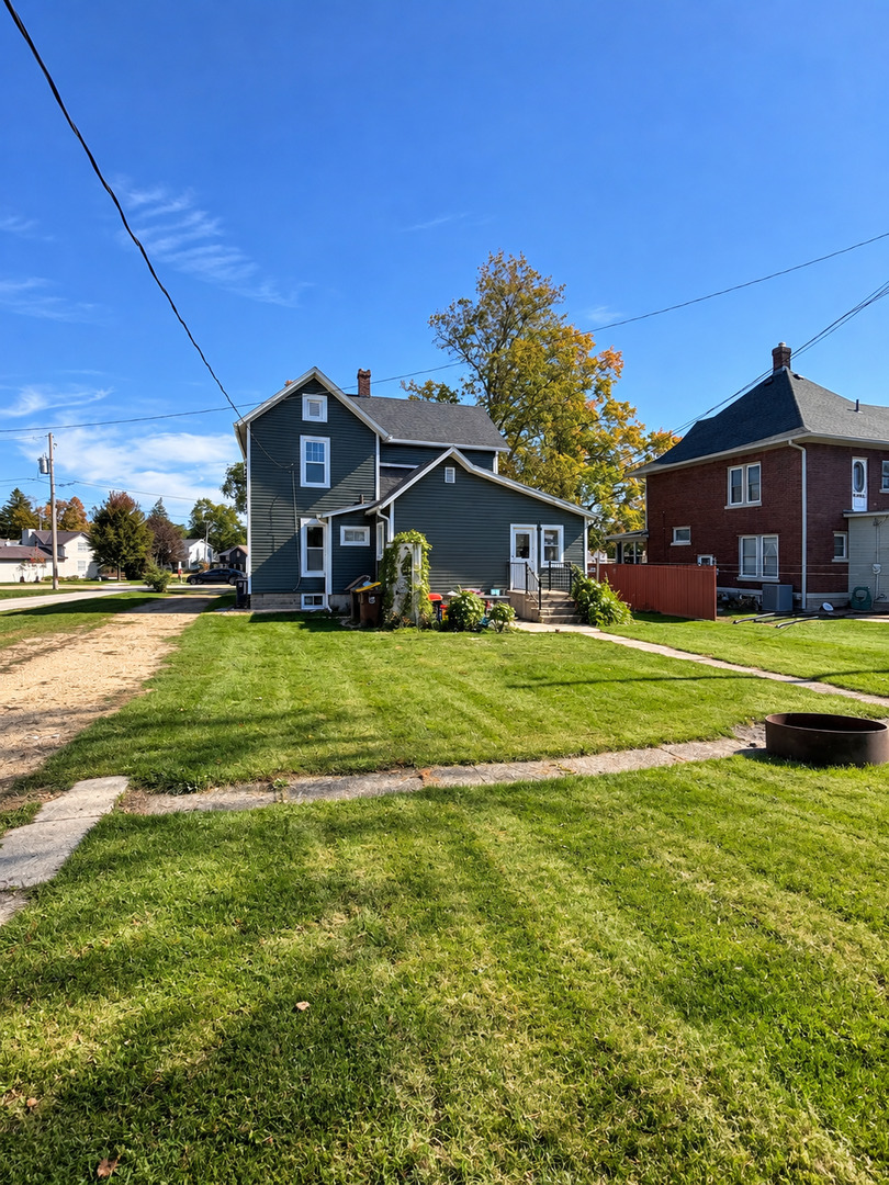 Dark green two-story house with a broad lawn and a small garden beside the entrance.