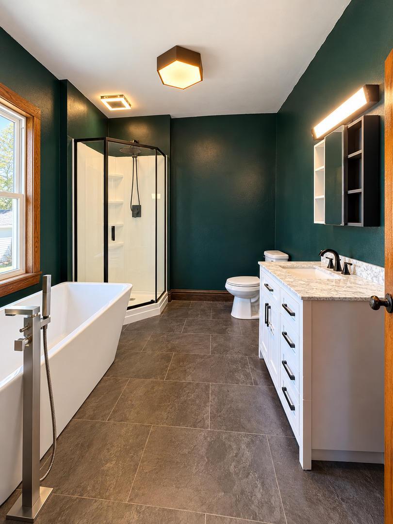 Bathroom with a freestanding tub, glass shower, and white vanity against deep green walls.