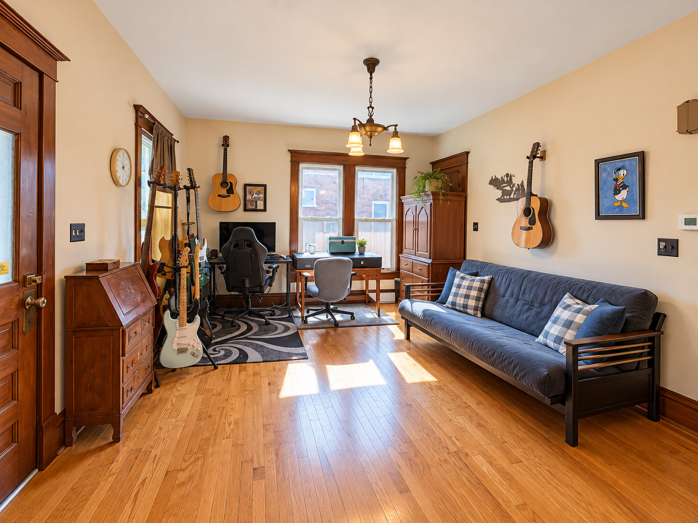 Music room with a blue sofa, guitars, desk, and warm wood floors.