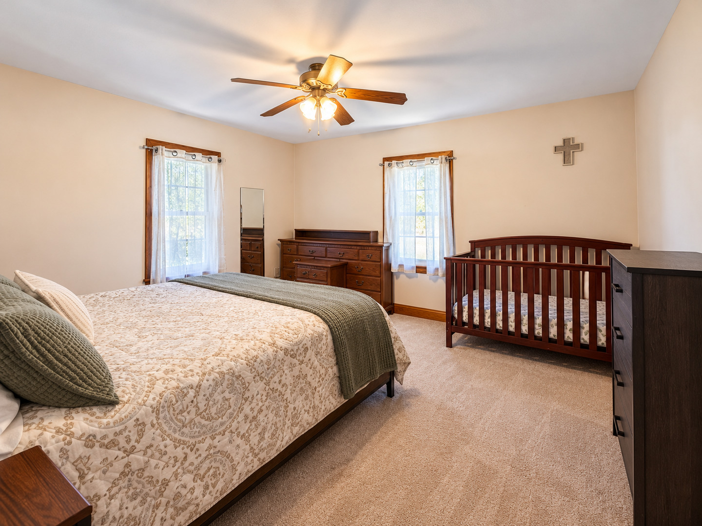 Furnished bedroom with a large bed, wooden crib, and ceiling fan.