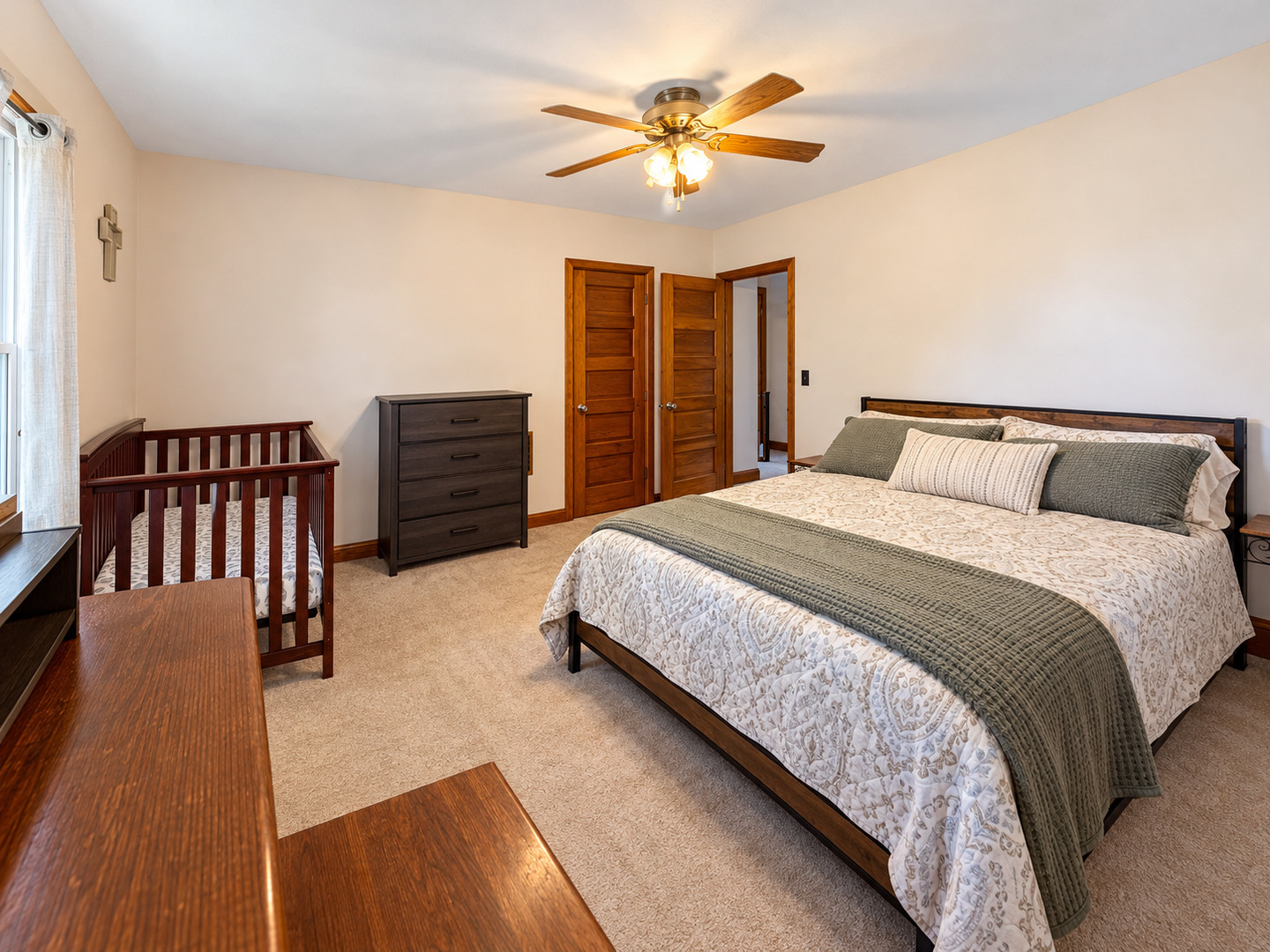 Bedroom with a large bed, wooden crib, and ceiling fan.