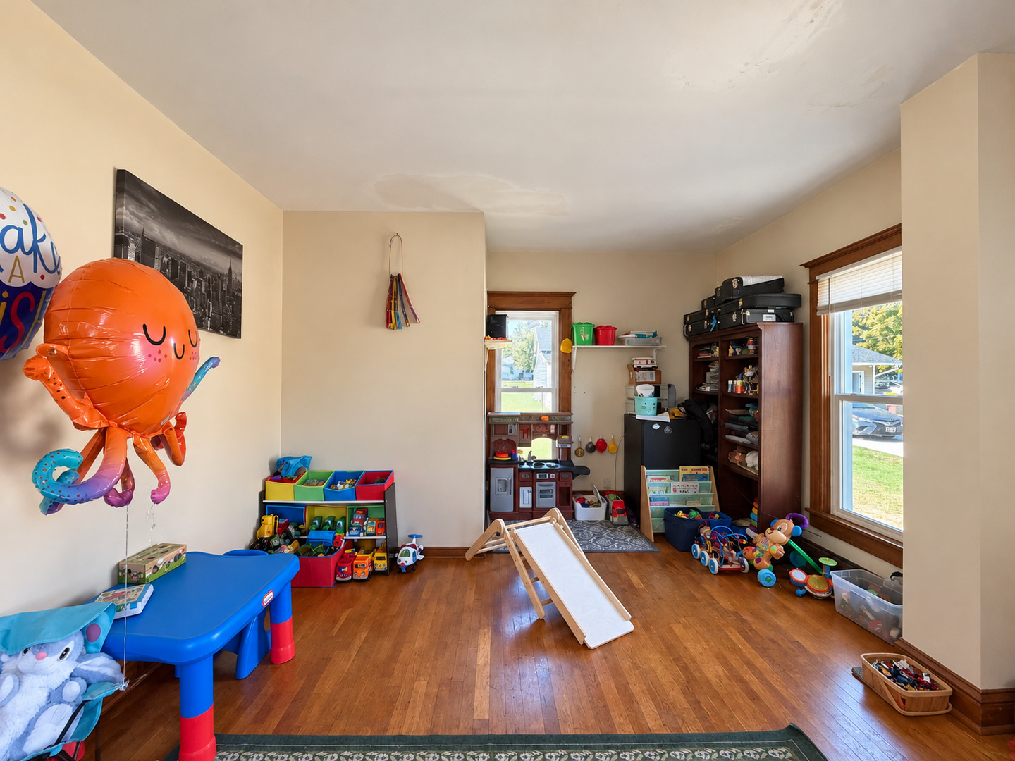 Playroom with a small slide, toy shelves, and wood flooring.