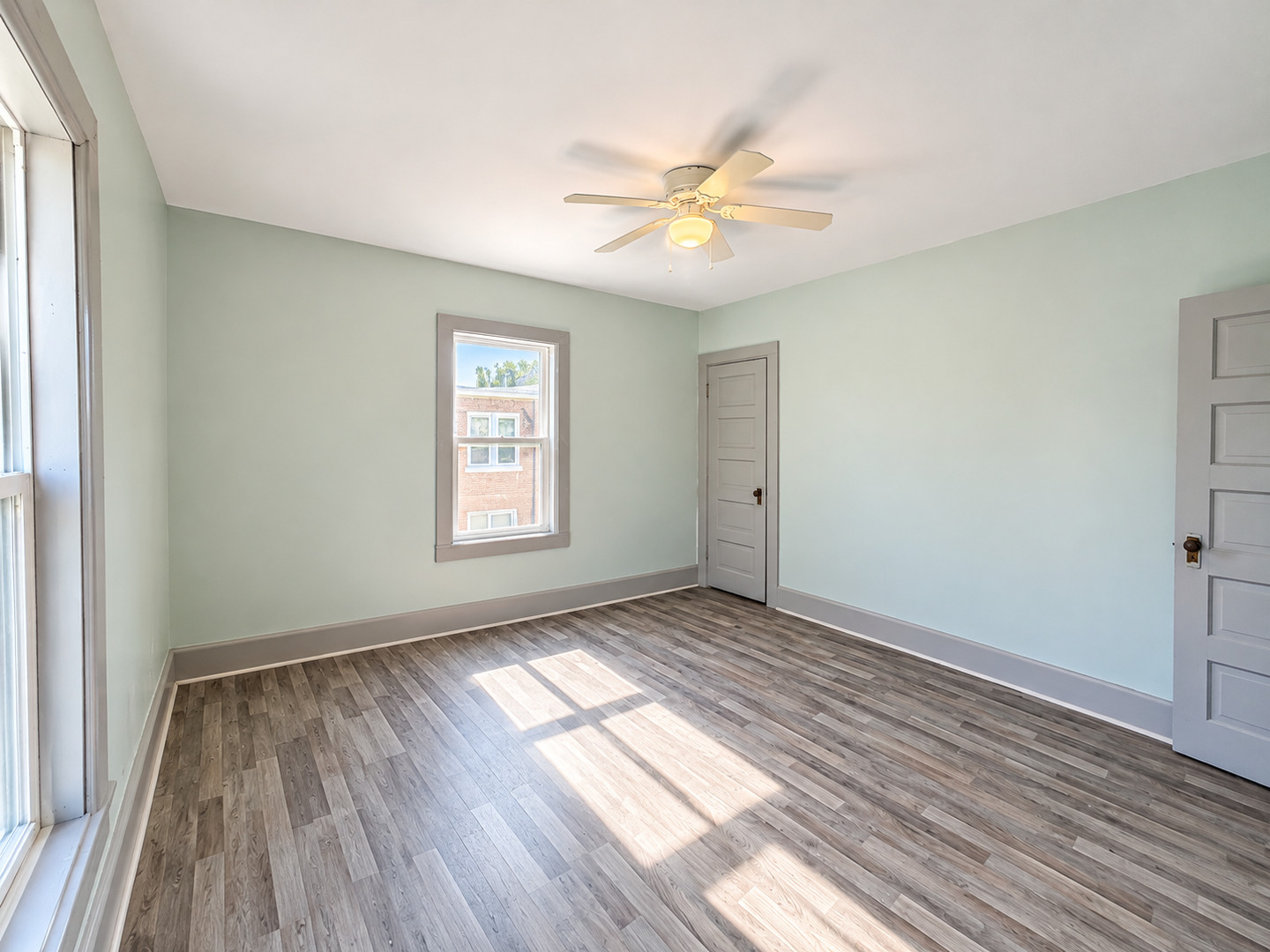 Vacant room with pale green walls, gray wood-look flooring, and a ceiling fan.