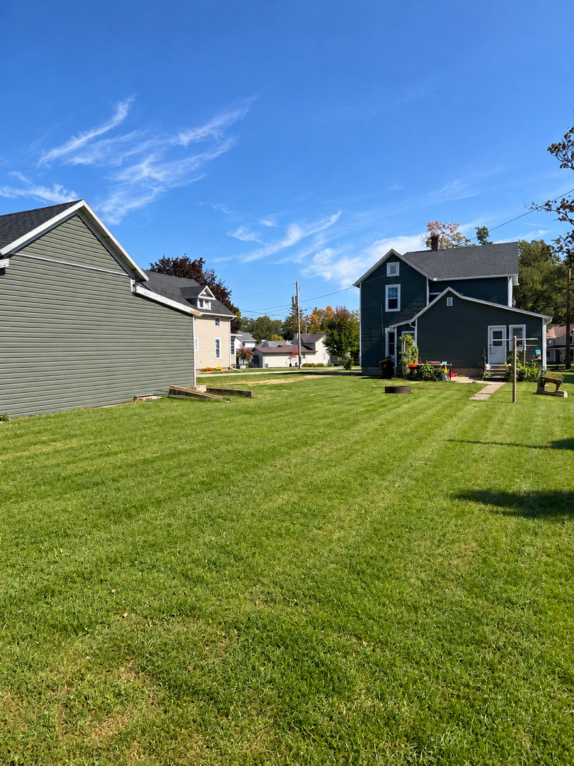 Backyard lawn behind a dark-sided house, with a paved path and neighboring homes.
