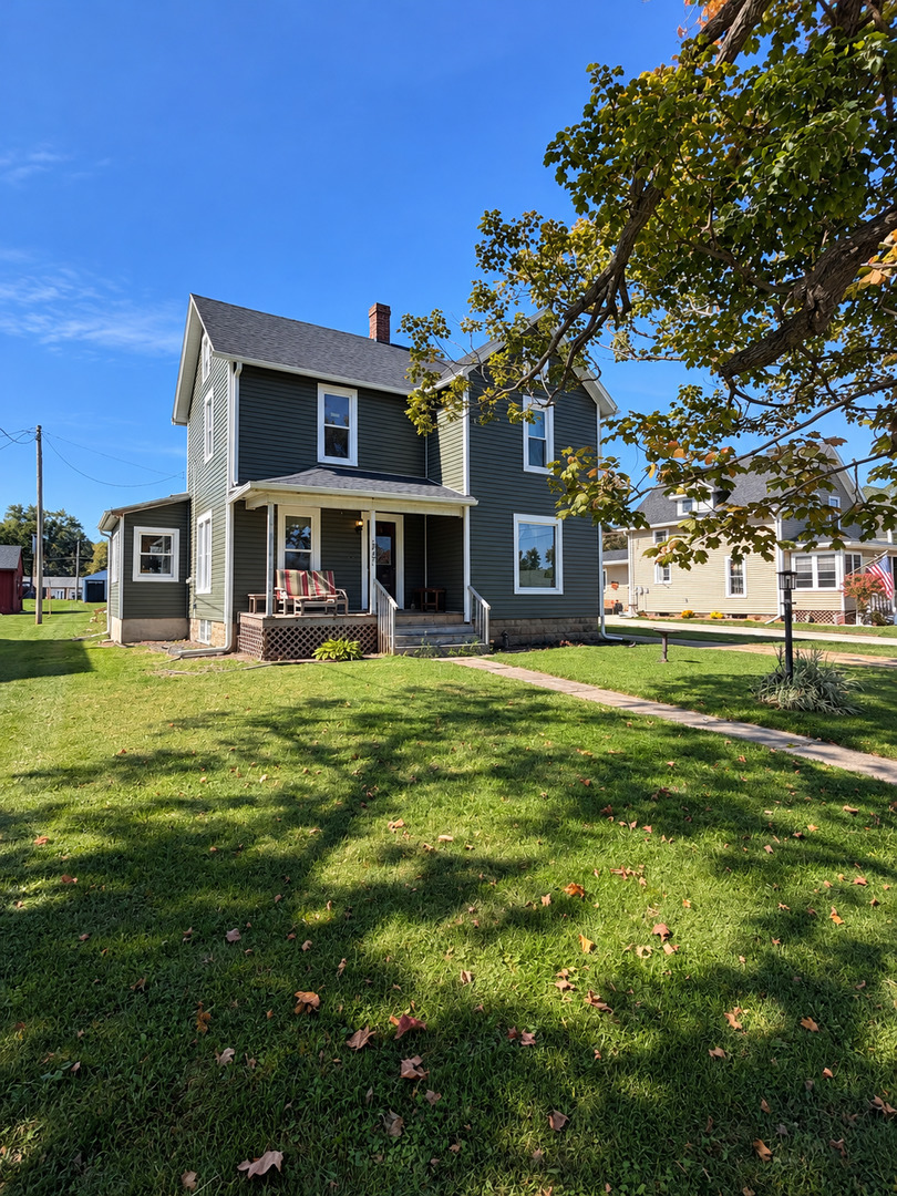 Two-story dark-sided house with a covered front porch and broad lawn.