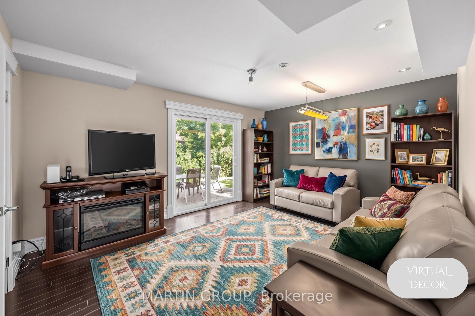 Virtually staged living room with cream sofas, a colorful geometric rug, and sliding doors to a leafy backyard.