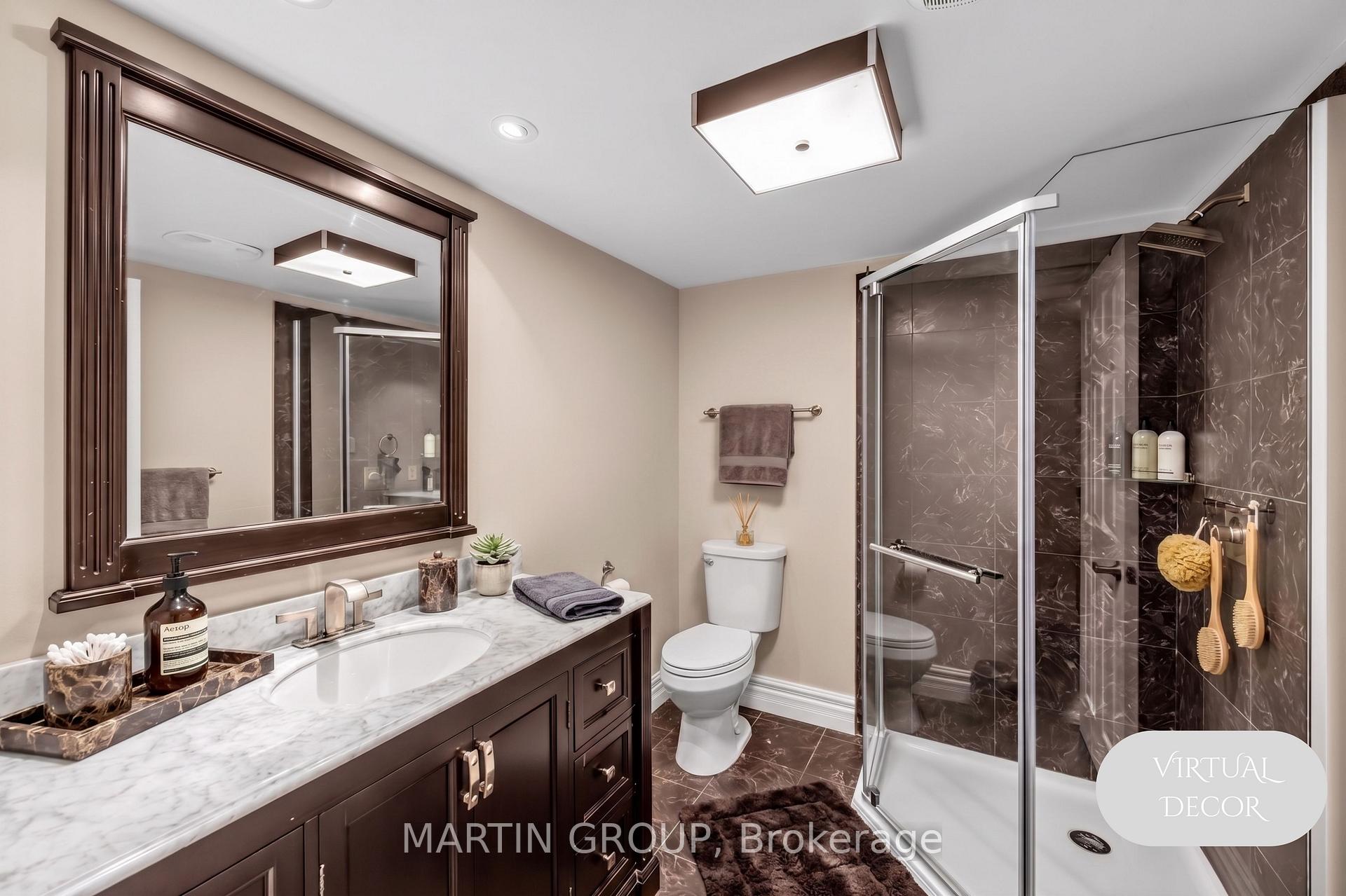 Bathroom with dark wood vanity, marble-look counter, framed mirror, and glass-enclosed dark-tile shower.