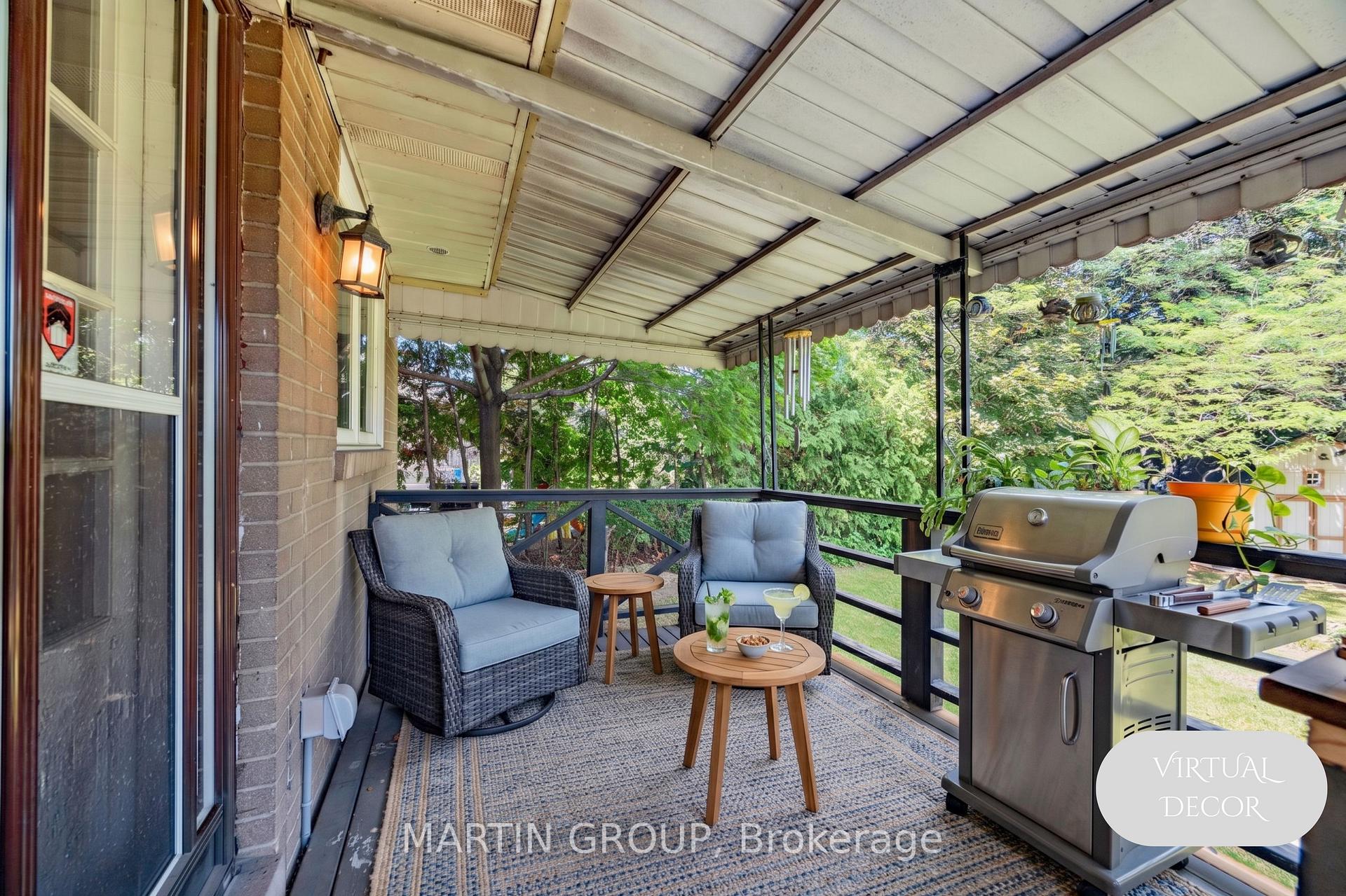 Covered patio with wicker seating and a stainless steel barbecue, surrounded by leafy greenery.