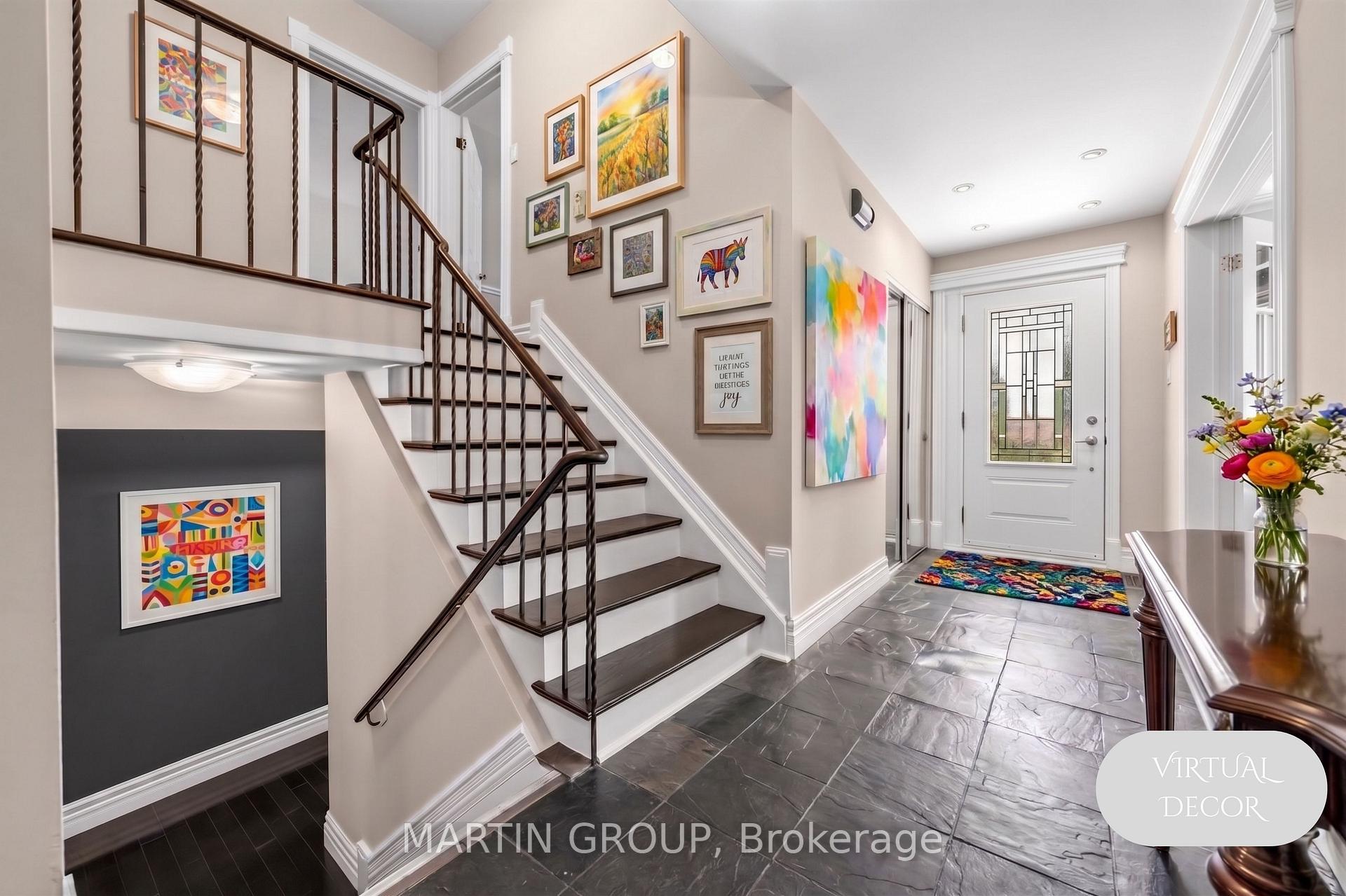 Home foyer with a dark-tread staircase, colorful gallery wall, gray tile floor, and decorative-glass entry door.