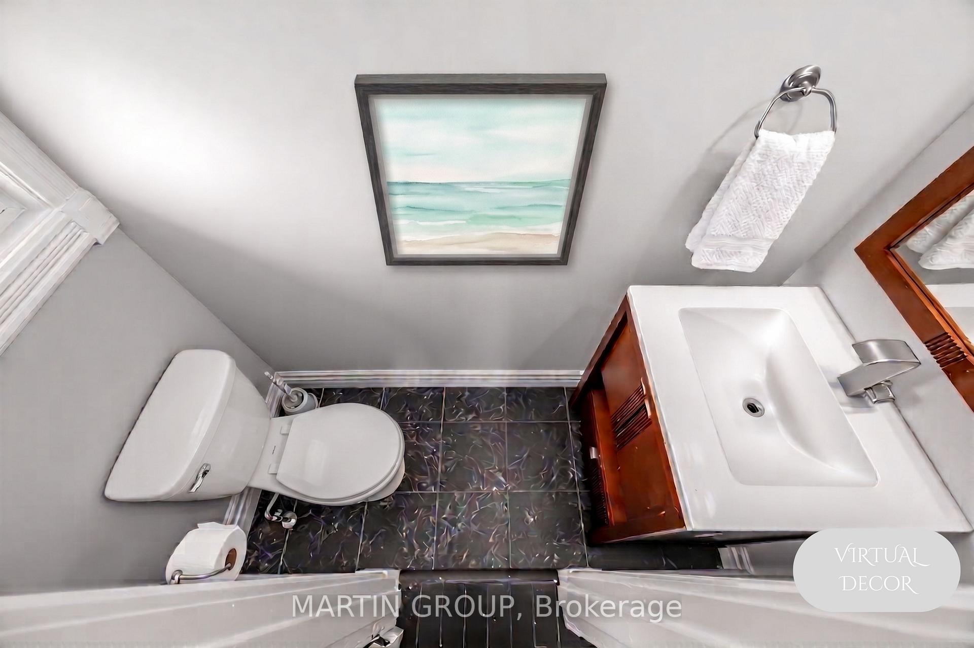 Bathroom with dark patterned floor tiles, white fixtures, wood vanity cabinet, and framed beach artwork.