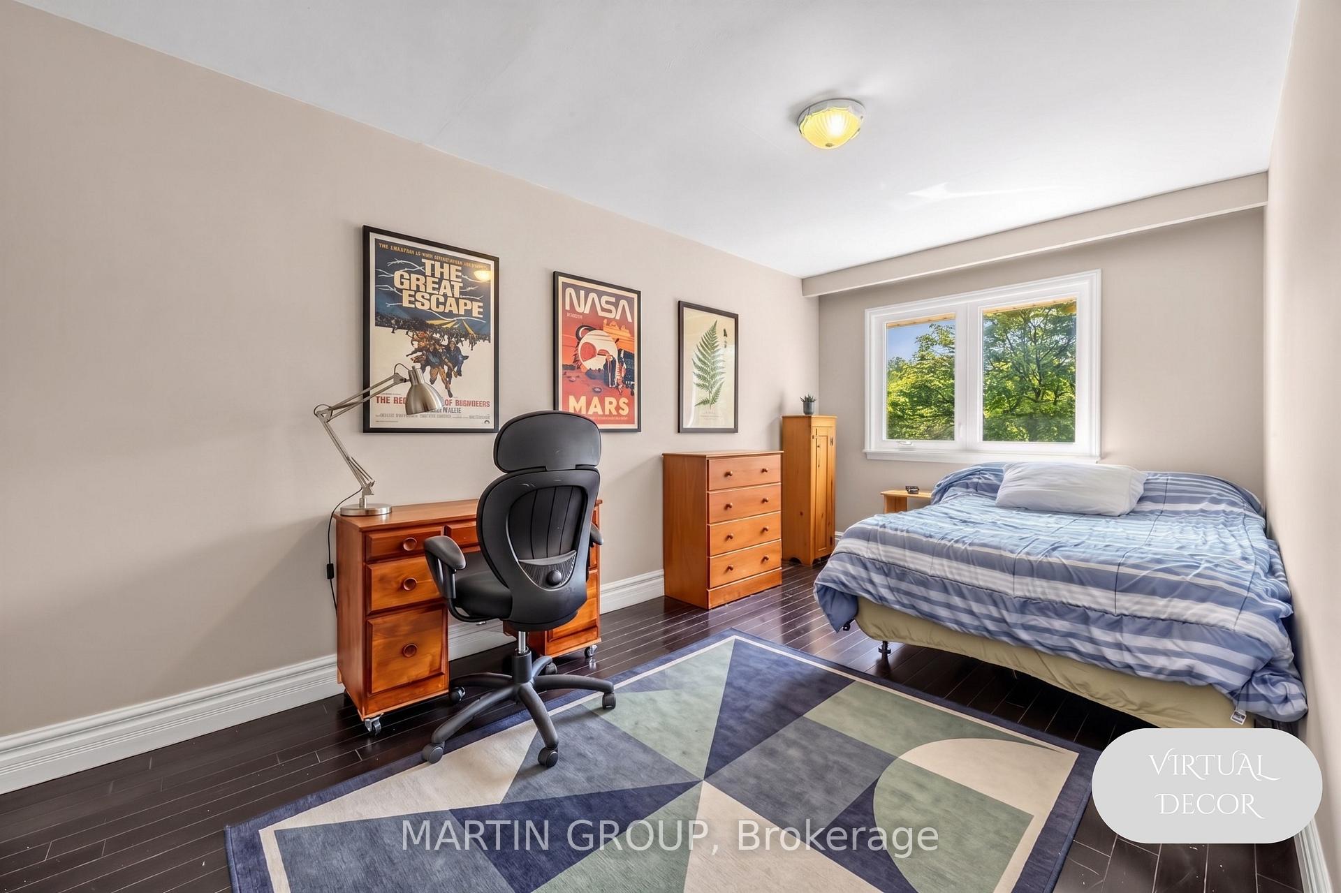 Bedroom with a striped bed, wooden desk, space posters, and a window overlooking leafy trees.