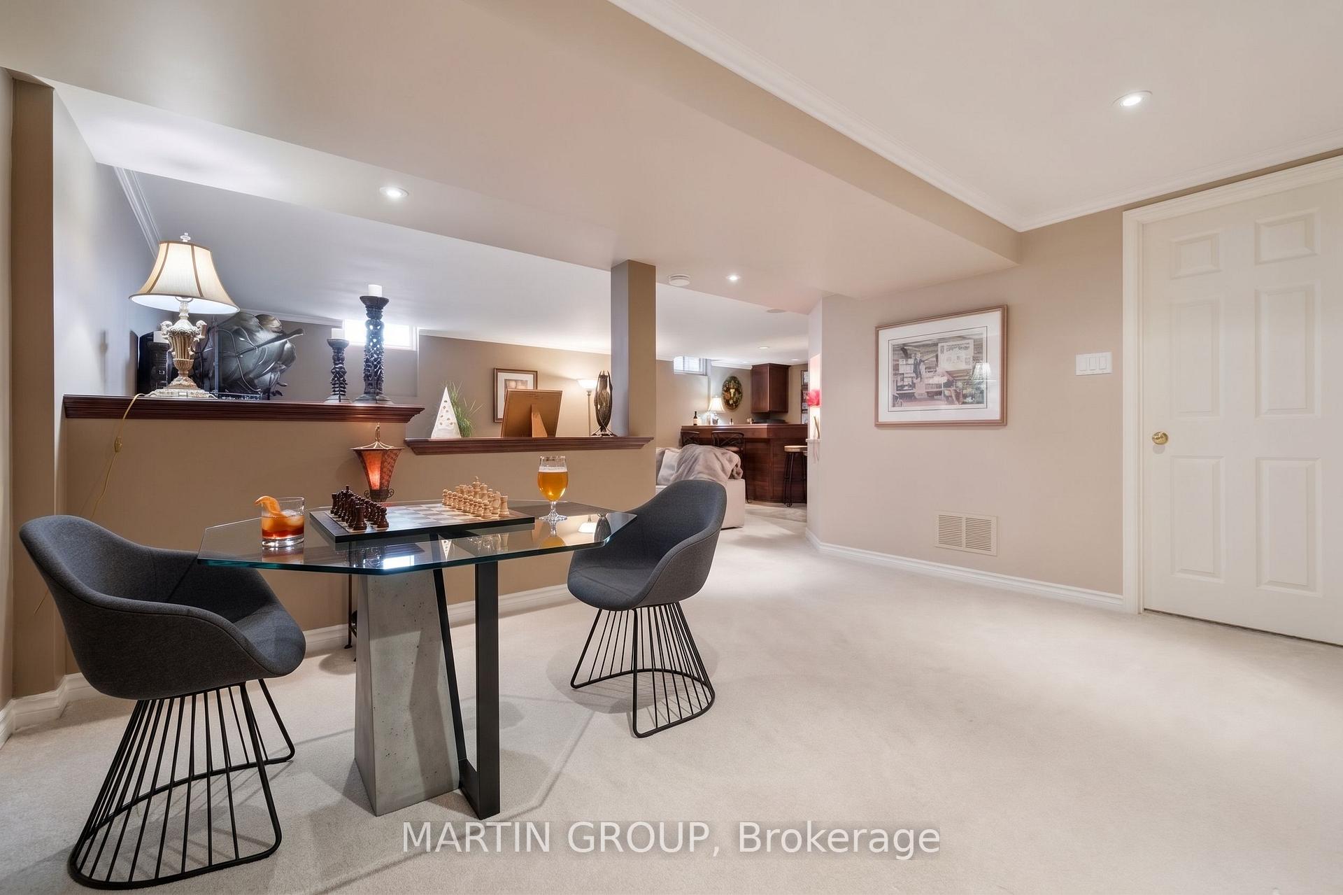 Basement recreation area with a glass chess table, gray chairs, and a bar in the background.
