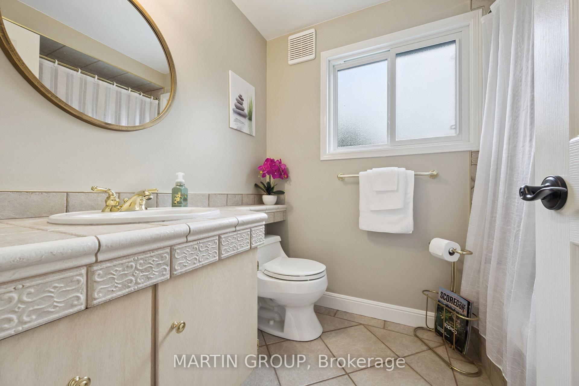 Bathroom with ornate tiled vanity, round mirror, frosted window, and purple orchid.