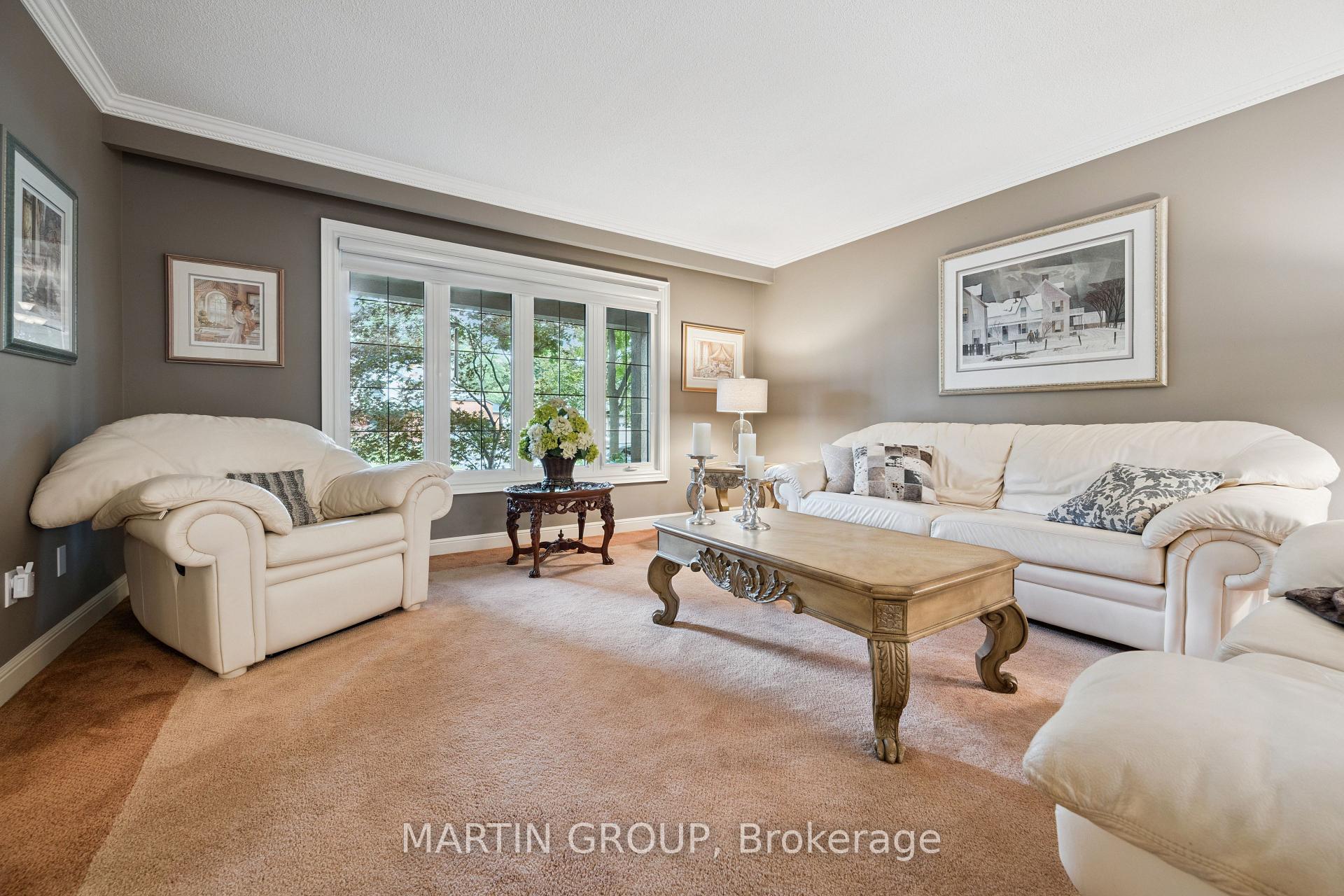 Living room with cream sofas, an ornate coffee table, and a large window overlooking trees.