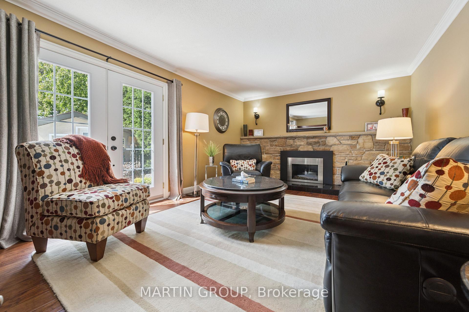 Living room with a stone fireplace, leather seating, patterned chair, and French doors.