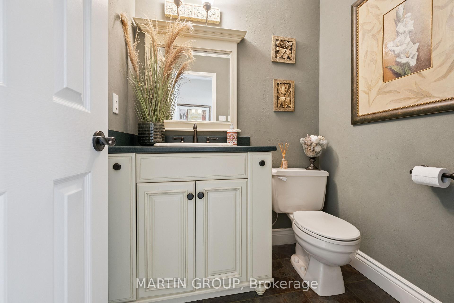 Powder room with a paneled white vanity, dark countertop, large mirror, and floral wall art.