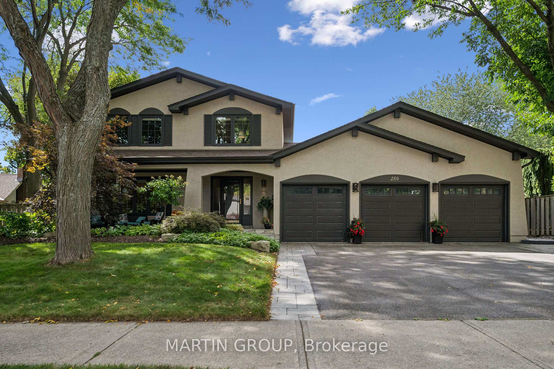 Two-story beige home with three-car garage, mature trees, and landscaped front yard.