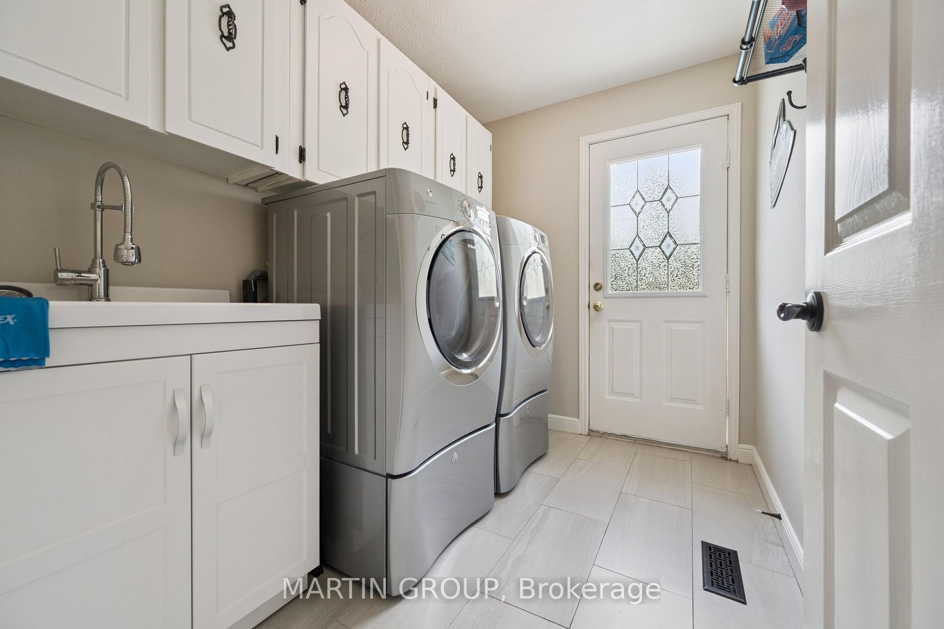 Laundry room with gray front-loading washer and dryer, white cabinets, and a utility sink.