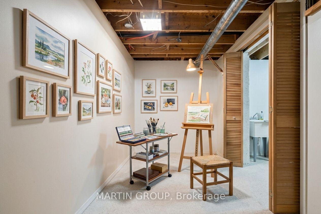Art studio with framed botanical prints, an easel, and art supplies beneath exposed wood beams.