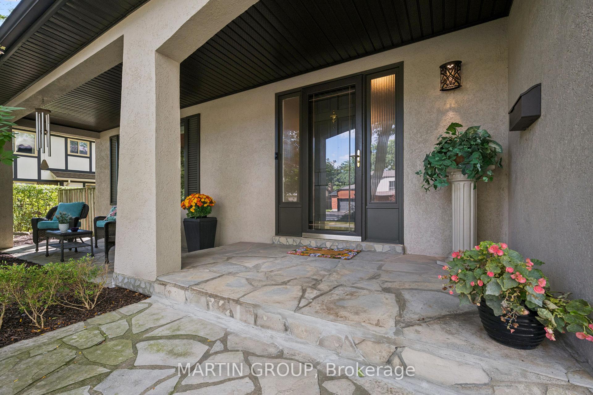 Covered front porch with a dark-framed glass door, stone paving, potted flowers, and outdoor seating.