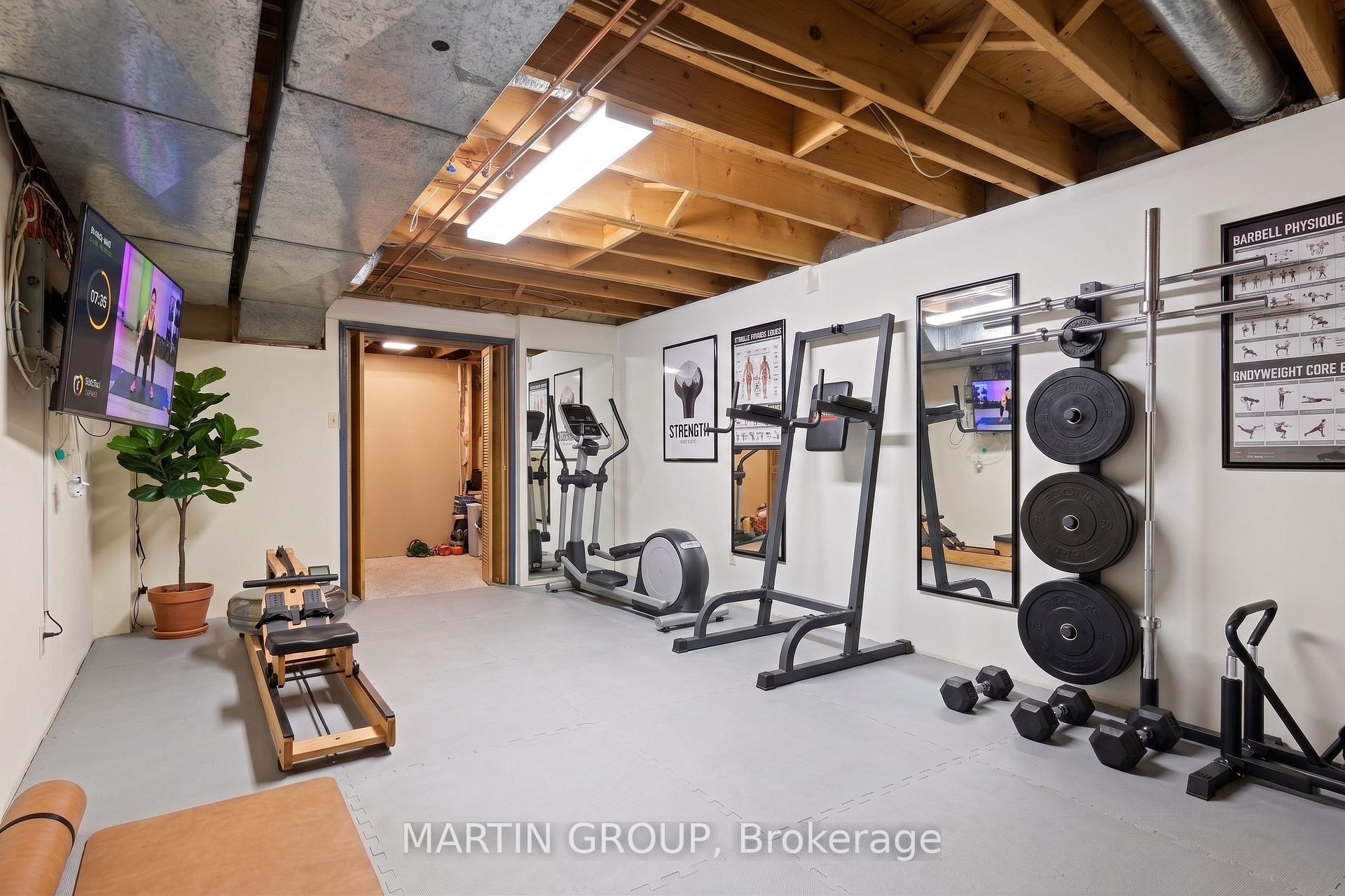 Home gym with weight racks, dumbbells, cardio equipment, mirrors, and exposed wooden ceiling beams.