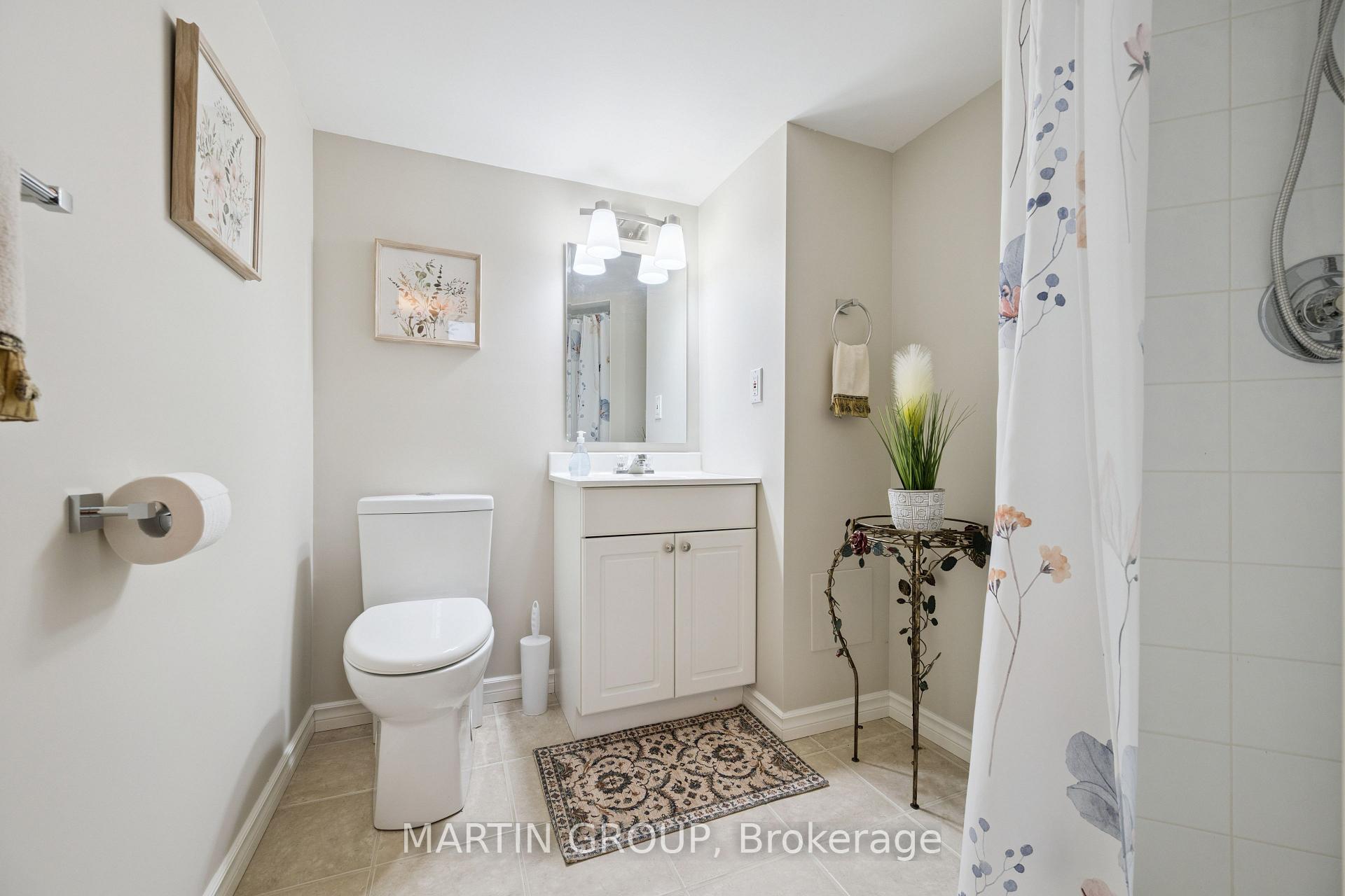 Bright bathroom with white vanity, toilet, floral shower curtain, and patterned floor rug.